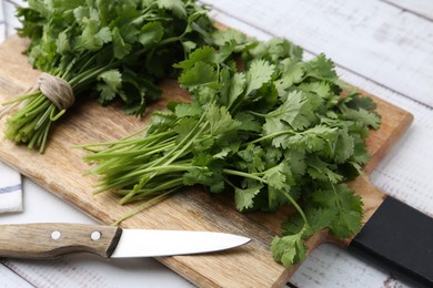 Photo of Cutting board with fresh cilantro and knife on white wooden table, closeup