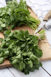 Photo of Cutting board with fresh cilantro and knife on white wooden table, closeup