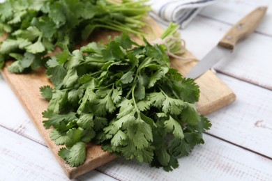 Photo of Cutting board with fresh cilantro and knife on white wooden table, closeup