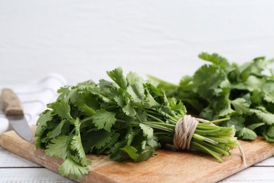 Photo of Cutting board with fresh cilantro and knife on white wooden table, closeup. Space for text