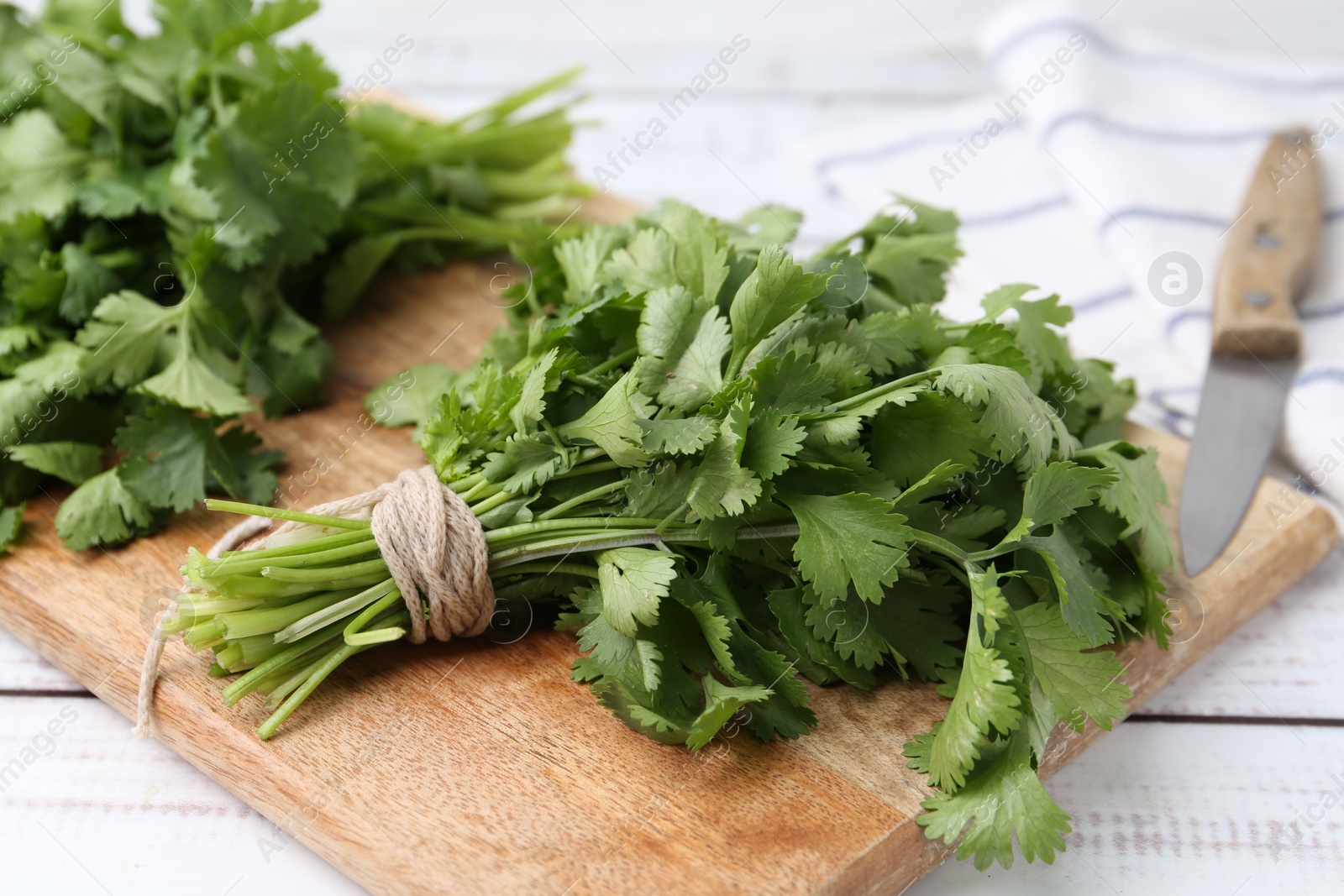 Cutting board with fresh cilantro and knife on white wooden table, closeup Photo of Cutting board with fresh cilantro and knife on white wooden table, closeup