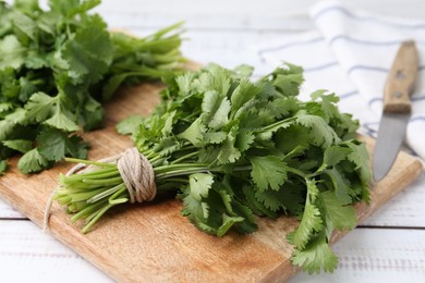 Photo of Cutting board with fresh cilantro and knife on white wooden table, closeup