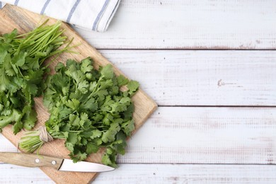 Photo of Cutting board with fresh cilantro and knife on white wooden table, top view. Space for text