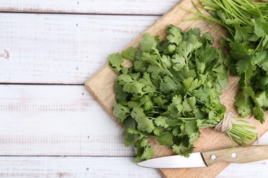 Photo of Cutting board with fresh cilantro and knife on white wooden table, top view. Space for text