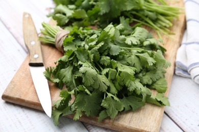Photo of Cutting board with fresh cilantro and knife on white wooden table, closeup