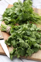 Photo of Cutting board with fresh cilantro and knife on white wooden table, closeup