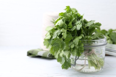 Photo of Fresh aromatic cilantro in jar on white table, closeup. Space for text