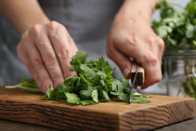 Photo of Woman cutting fresh cilantro at wooden table, closeup