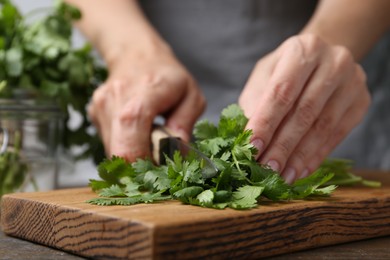 Photo of Woman cutting fresh cilantro at wooden table, closeup