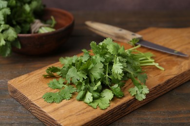 Photo of Cutting board with fresh cilantro and knife on wooden table, closeup