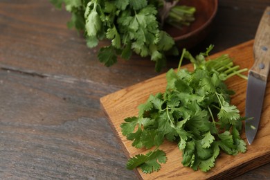 Photo of Cutting board with fresh cilantro and knife on wooden table, closeup. Space for text