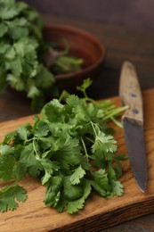 Photo of Cutting board with fresh cilantro and knife on wooden table, closeup