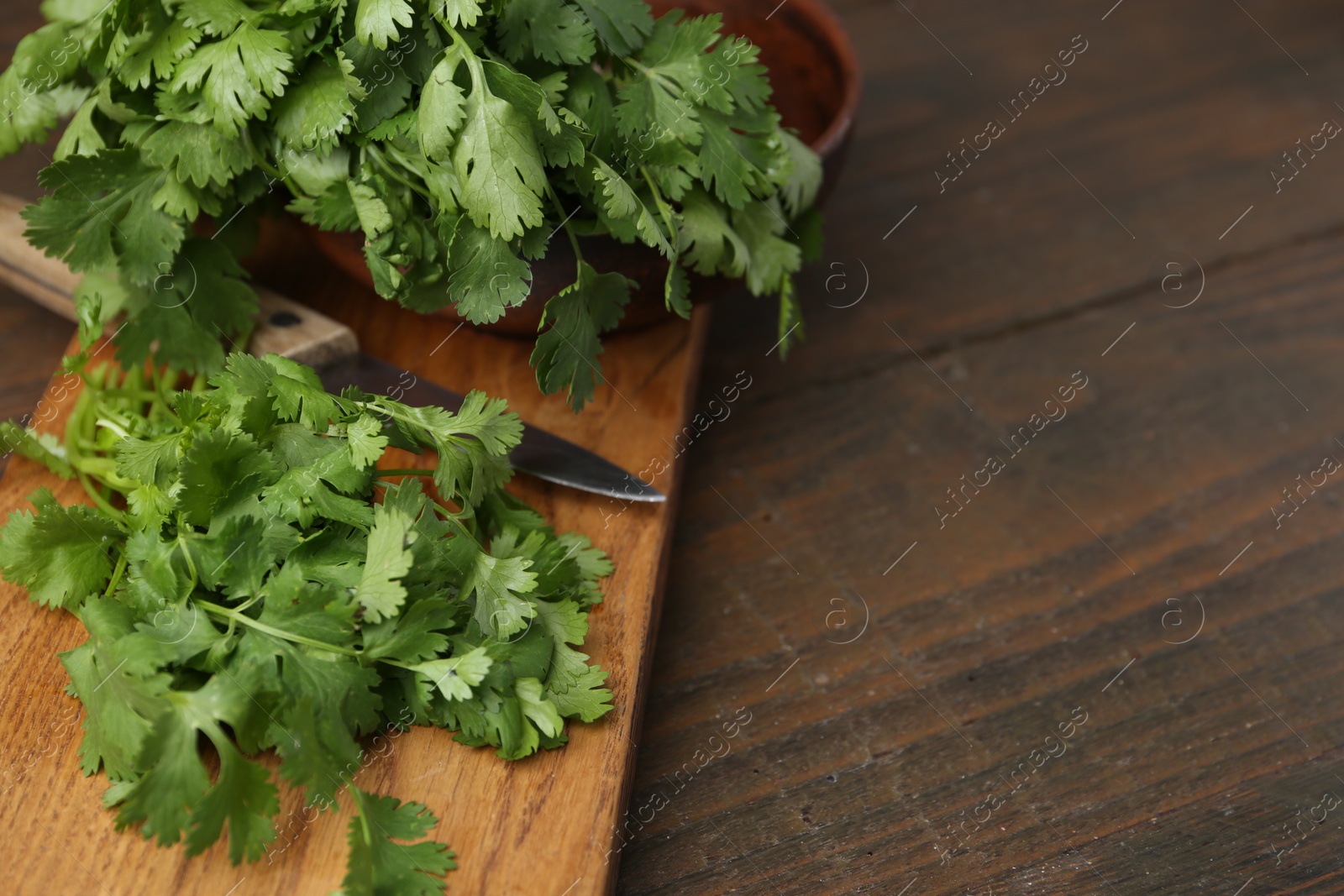 Photo of Cutting board with fresh cilantro and knife on wooden table, closeup. Space for text