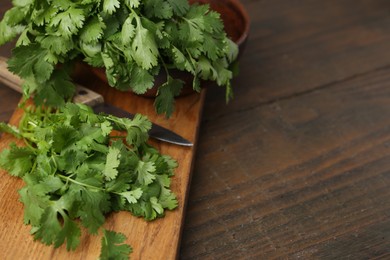 Photo of Cutting board with fresh cilantro and knife on wooden table, closeup. Space for text