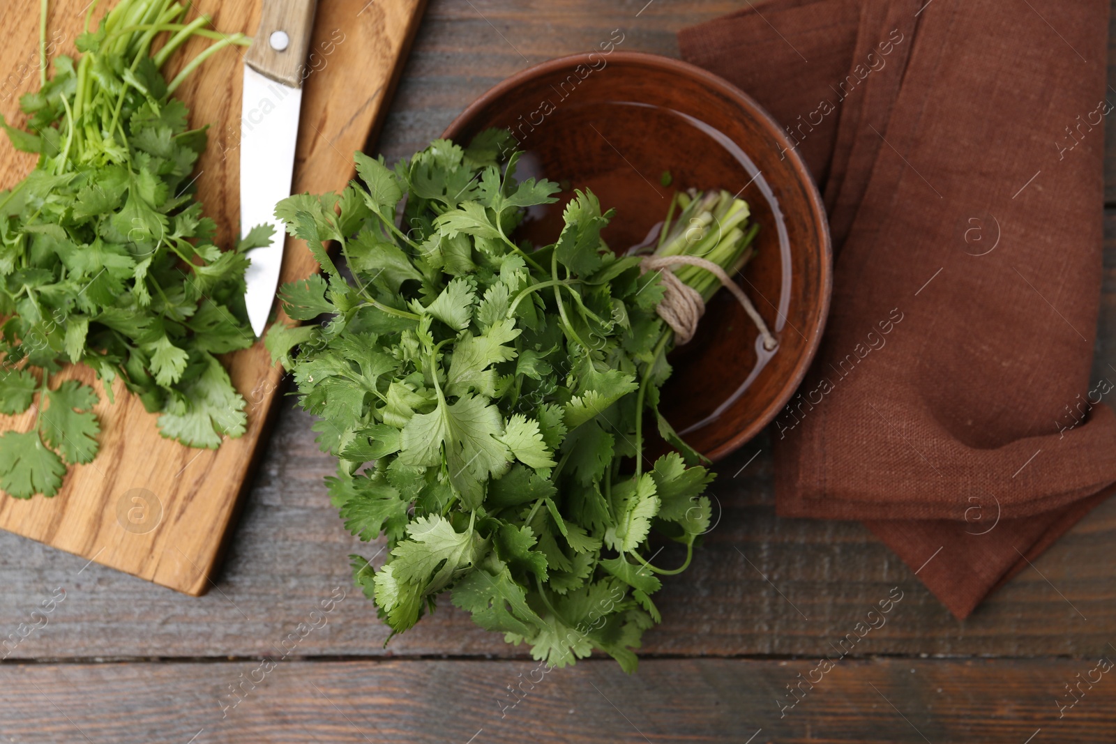 Photo of Cutting board with fresh cilantro and knife on wooden table, flat lay