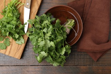 Photo of Cutting board with fresh cilantro and knife on wooden table, flat lay