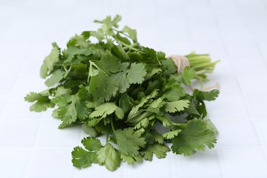 Photo of Fresh aromatic cilantro on white tiled table, closeup