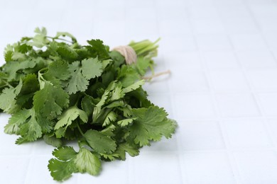 Photo of Fresh aromatic cilantro on white tiled table, closeup. Space for text