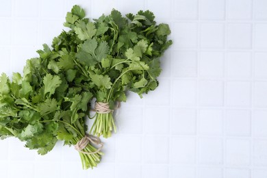 Photo of Fresh aromatic cilantro on white tiled table, top view. Space for text