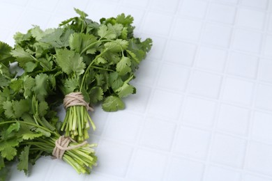 Photo of Fresh aromatic cilantro on white tiled table, closeup. Space for text