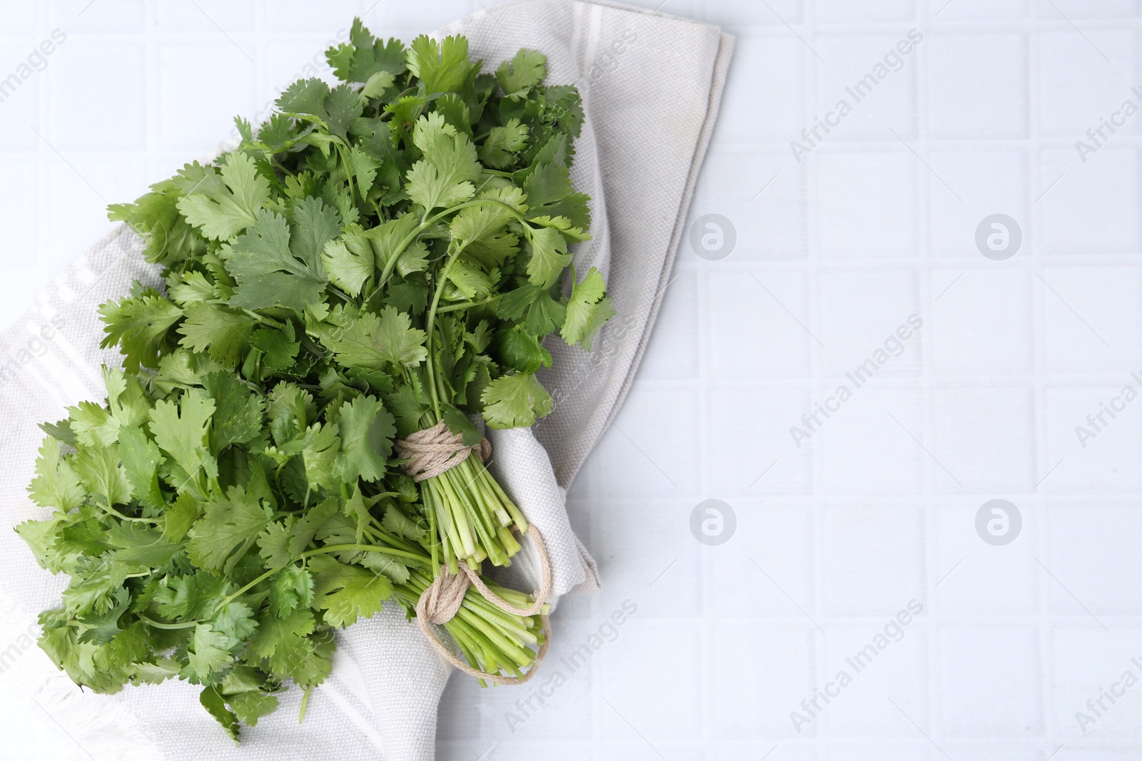 Photo of Fresh aromatic cilantro on white tiled table, top view. Space for text