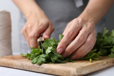 Photo of Woman cutting fresh cilantro at white table, closeup
