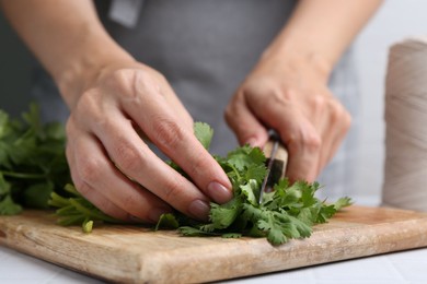 Photo of Woman cutting fresh cilantro at white table, closeup