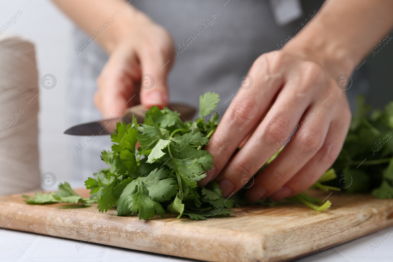 Photo of Woman cutting fresh cilantro at white table, closeup