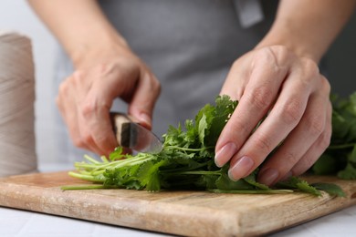 Photo of Woman cutting fresh cilantro at white table, closeup