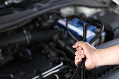 Photo of Auto mechanic with timing belt near open hood of car indoors, closeup. Space for text