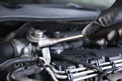 Photo of Auto parts. Professional mechanic with torque wrench fixing car indoors, closeup