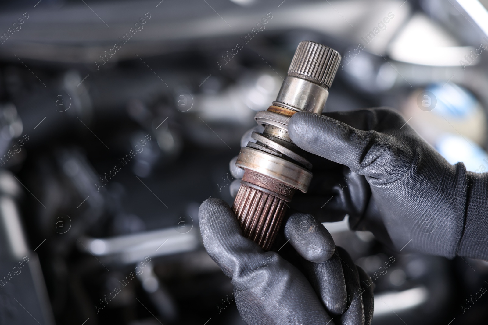 Auto part. Professional mechanic with drive shaft near open hood of car indoors, closeup. Space for text Photo of Auto part. Professional mechanic with drive shaft near open hood of car indoors, closeup. Space for text