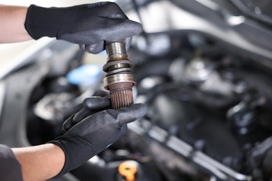 Photo of Auto part. Professional mechanic with drive shaft near open hood of car indoors, closeup. Space for text