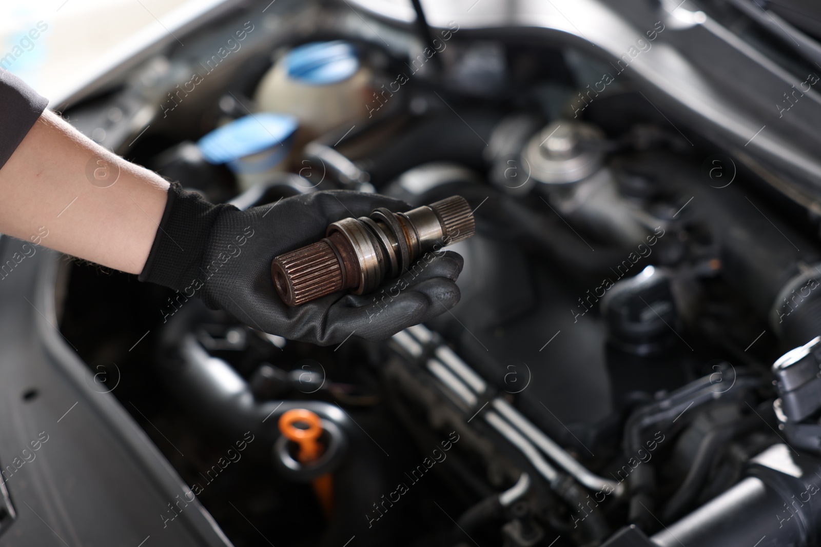Auto part. Professional mechanic with drive shaft near open hood of car indoors, closeup. Space for text Photo of Auto part. Professional mechanic with drive shaft near open hood of car indoors, closeup. Space for text
