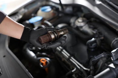 Photo of Auto part. Professional mechanic with drive shaft near open hood of car indoors, closeup. Space for text
