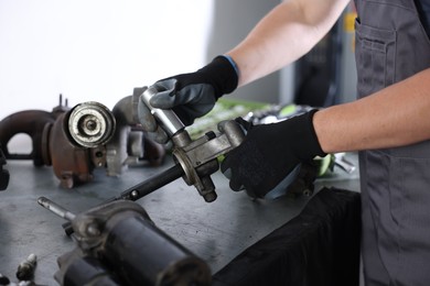 Photo of Auto parts. Professional mechanic fixing manual transmission at grey table indoors, closeup