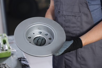 Photo of Auto parts. Professional mechanic with brake disc indoors, closeup