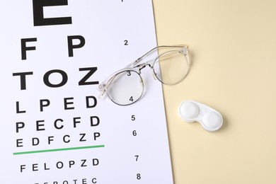 Photo of Vision test chart, glasses and lenses on beige background, above view