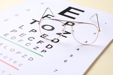 Photo of Vision test chart and glasses on beige background, closeup