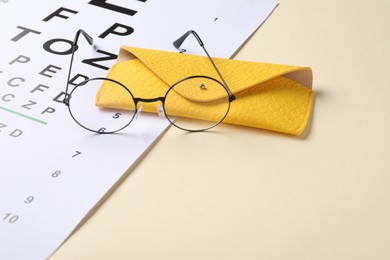 Photo of Vision test chart and glasses on beige background, closeup