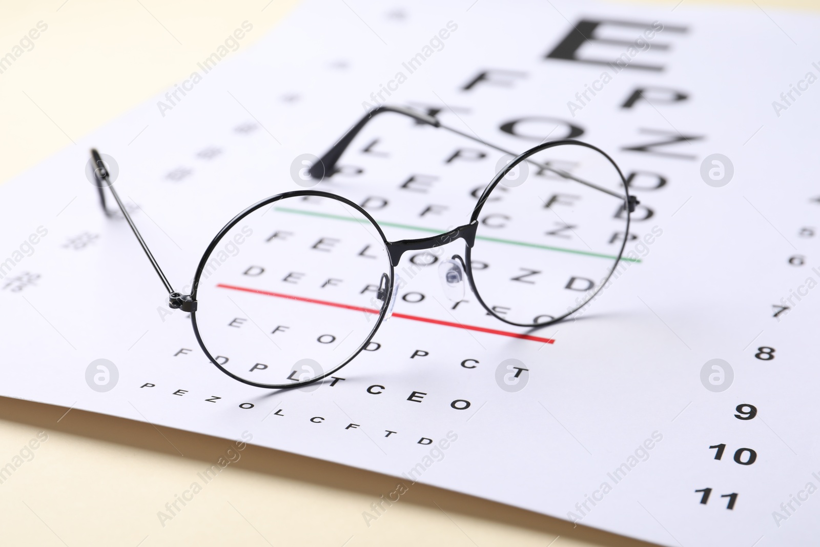 Photo of Vision test chart and glasses on beige background, closeup