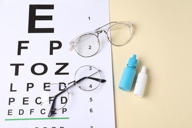 Photo of Vision test chart, glasses and bottles of medical drops on beige background, above view