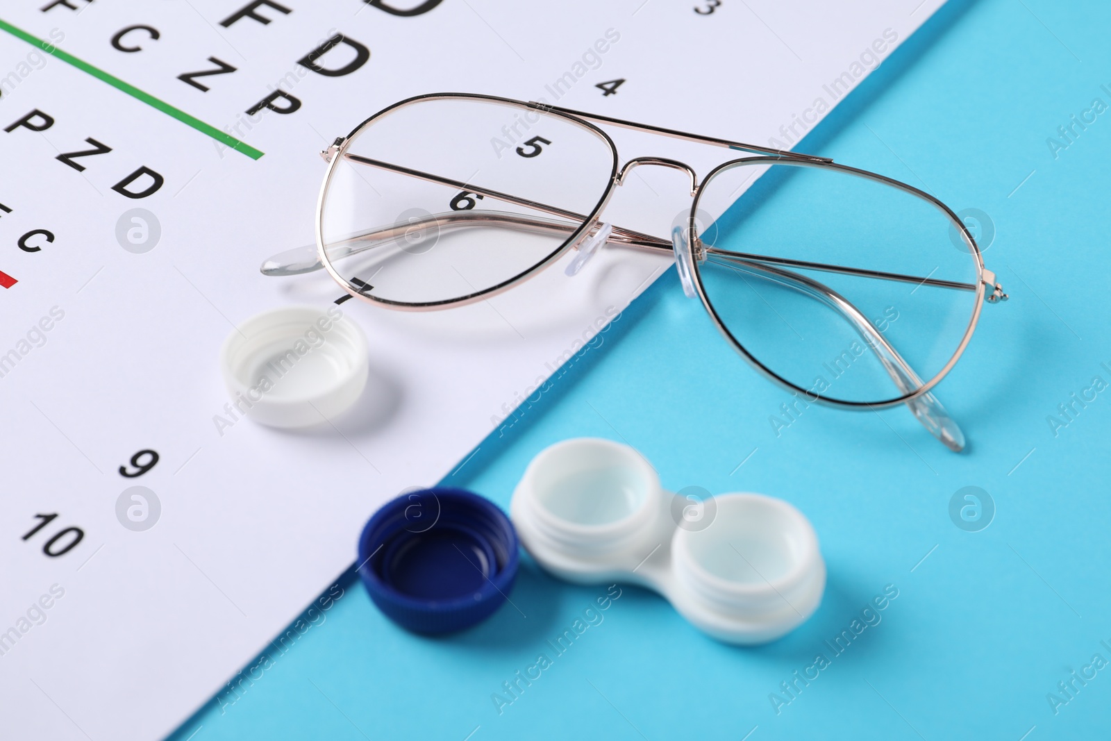 Photo of Vision test chart, glasses and lenses on light blue background, closeup