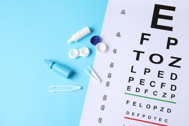 Photo of Vision test chart, tweezers, lenses and bottles of medical drops on light blue background, above view
