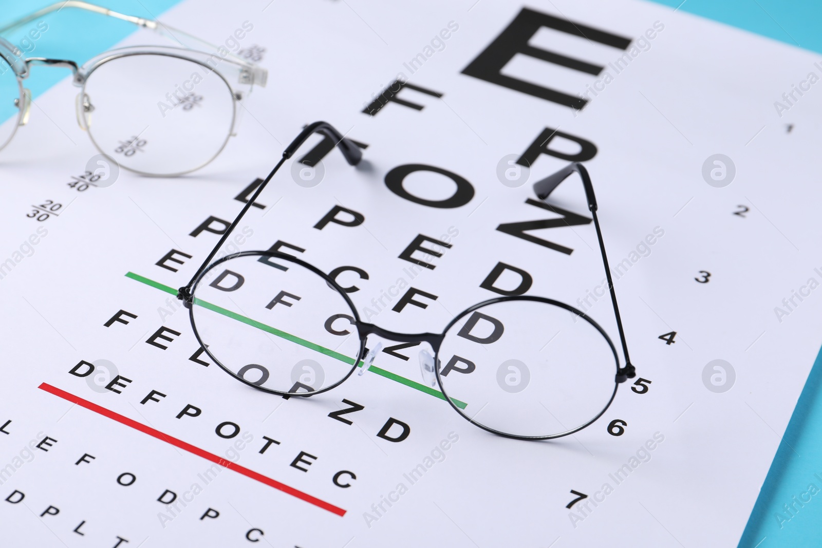 Vision test chart and glasses on light blue background, closeup Photo of Vision test chart and glasses on light blue background, closeup