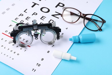 Photo of Vision test chart, glasses, trial frame and bottles of medical drops on light blue background, above view