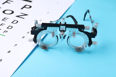 Photo of Vision test chart and trial frame on light blue background, closeup