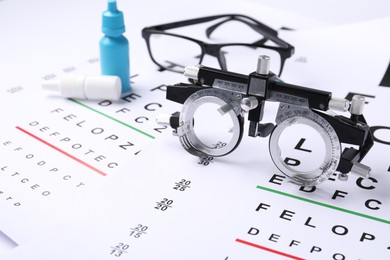 Photo of Glasses, trial frame and bottles of medical drops on vision test charts, closeup