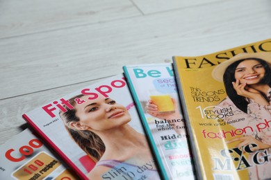 Photo of Different trendy magazines on white wooden table, closeup. Space for text