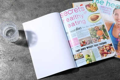 Photo of Trendy magazines and glass of water on grey background. Mockup for design